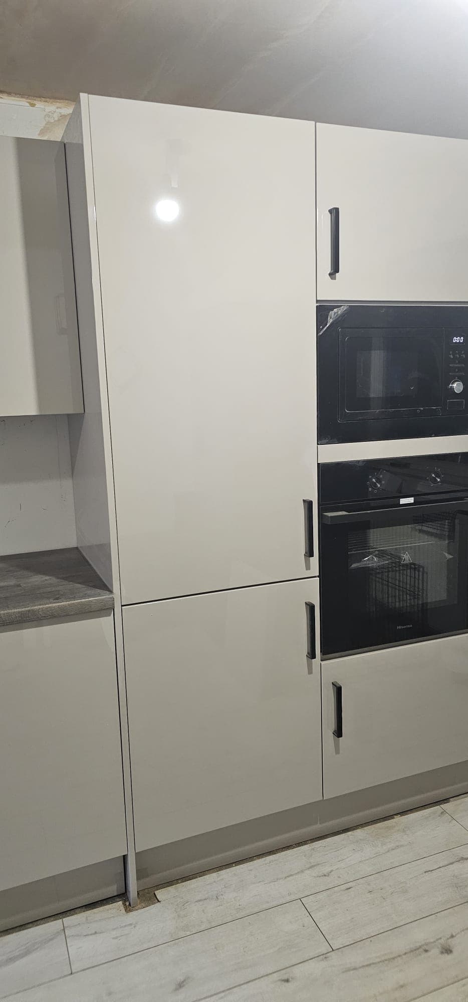Cream two-tone kitchen with white upper cabinets, dark integrated appliances, and chrome handles under ceiling downlights.