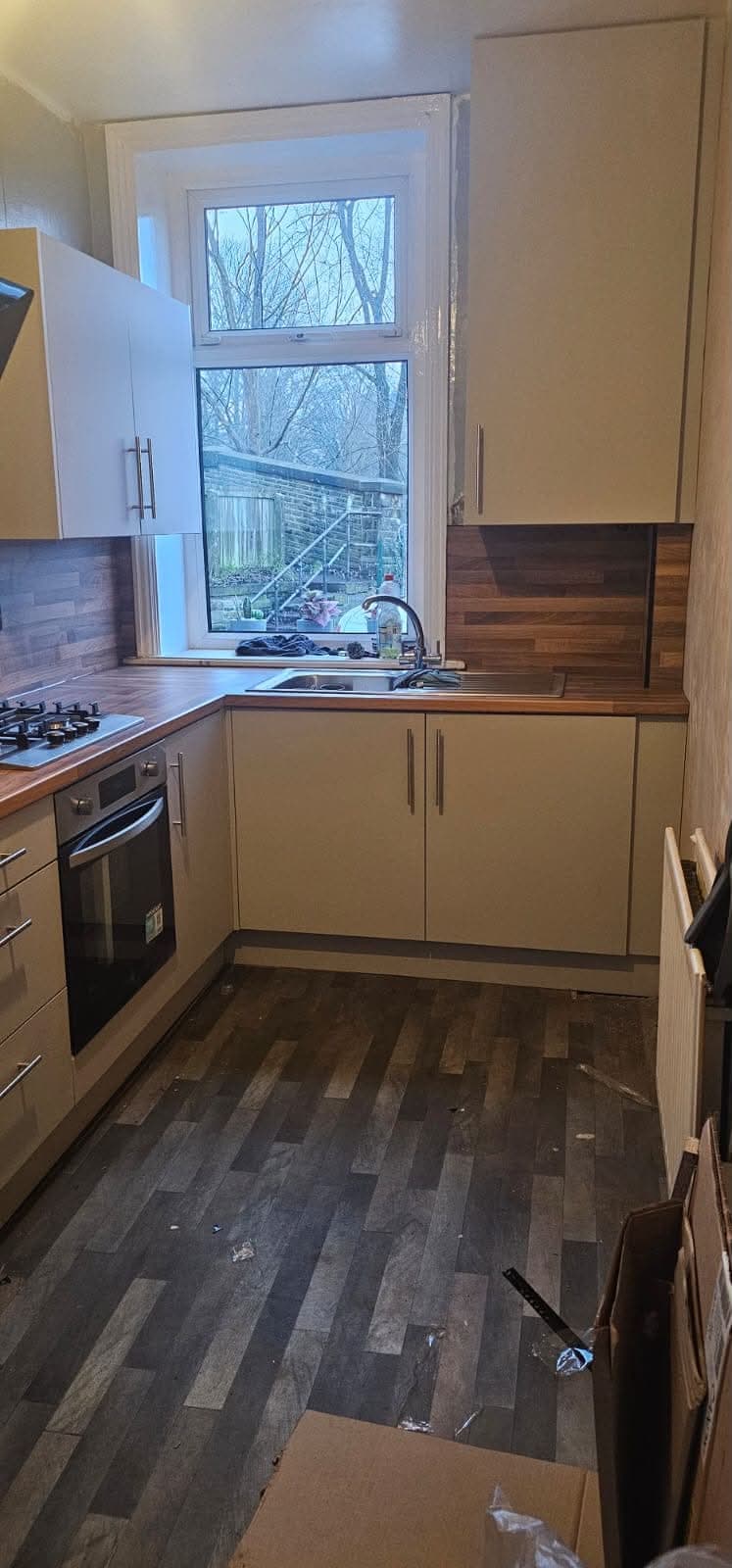 Cream modern kitchen with walnut worktop, dark backsplash, window sink, cream cabinets, and dark vinyl flooring.