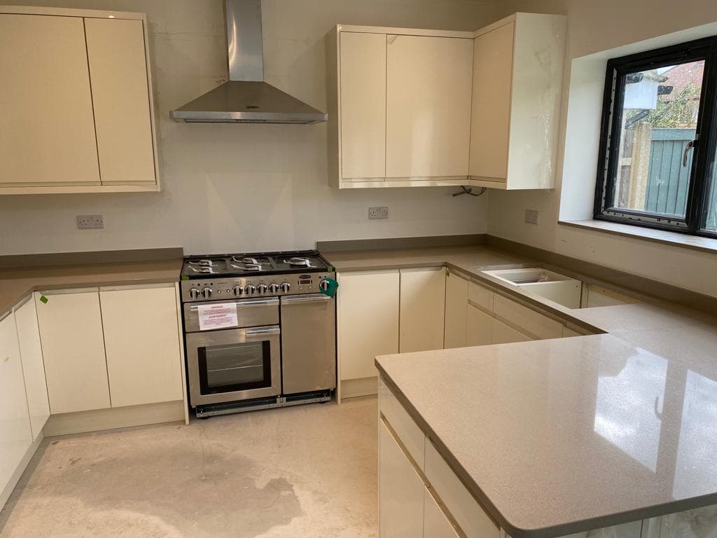 Cream-coloured shaker-style kitchen with light-tone worktops, U-shaped layout, range cooker, and island with seating space.
