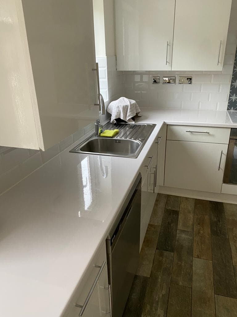 Cream shaker-style galley kitchen with white quartz worktops, stainless steel sink, and dark wood-effect flooring.