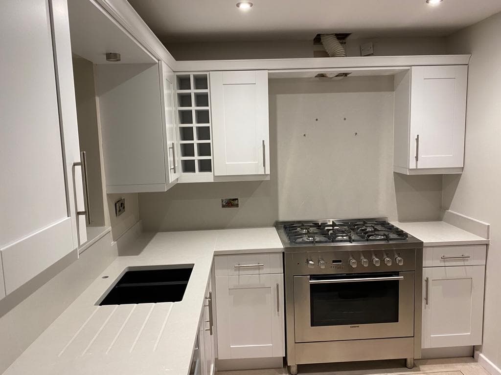 White shaker-style galley kitchen with cream stone worktops, stainless steel range cooker, and integrated appliances including induction hob.