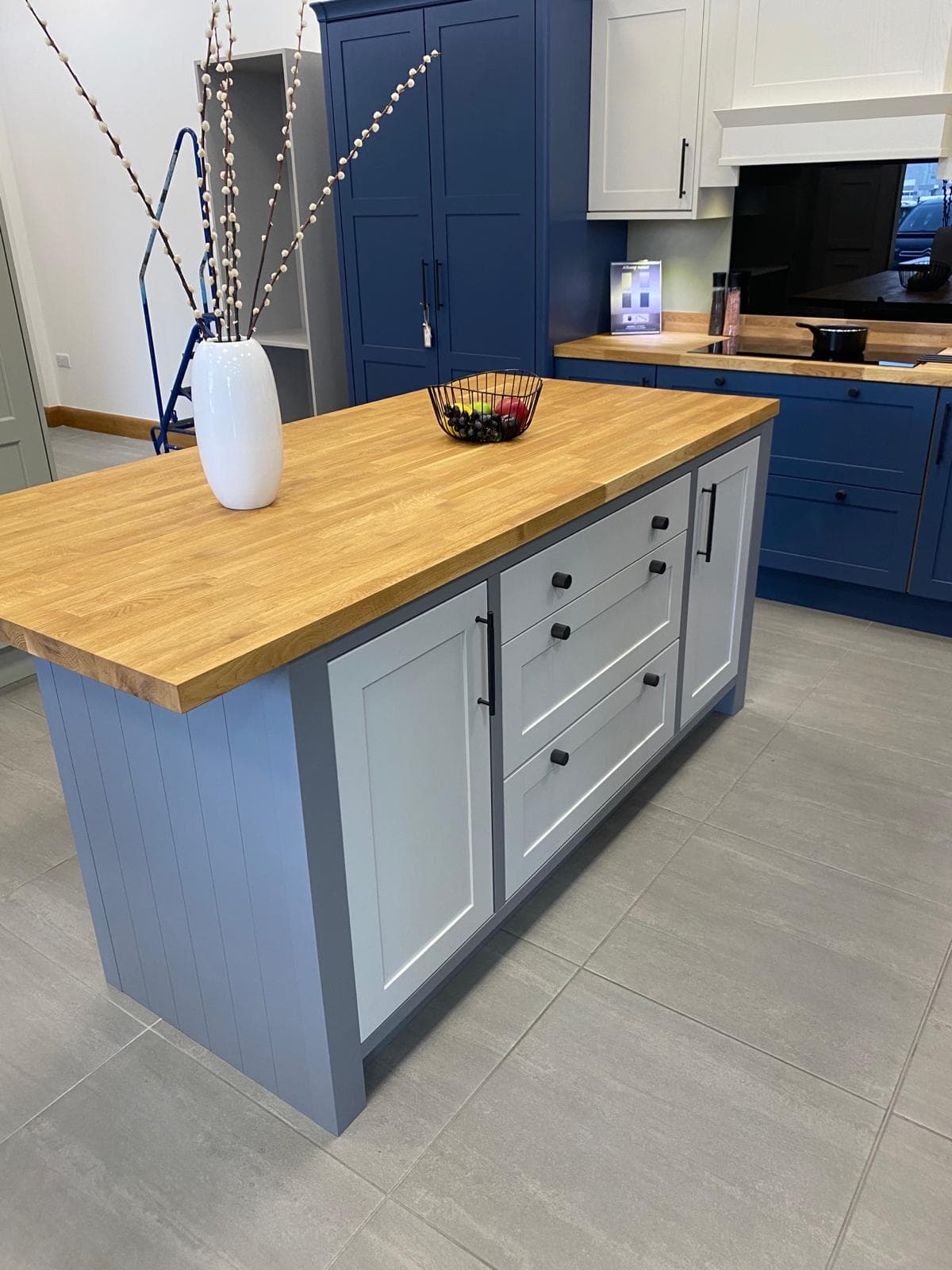 Two-tone shaker kitchen with navy blue cabinetry, white island base, and warm wooden worktops, featuring an island with seating space and matching navy wall units.
