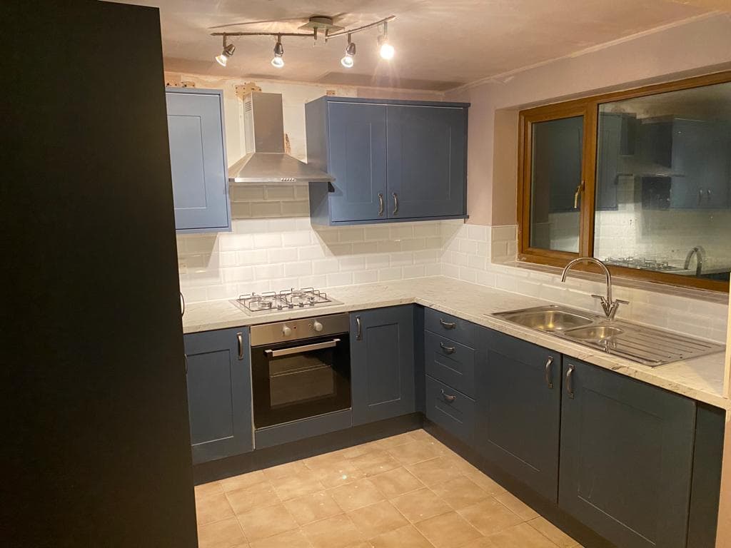 L-shaped kitchen with dark navy shaker cabinets, white subway tile splashback, and cream stone worktop with integrated sink and gas hob.