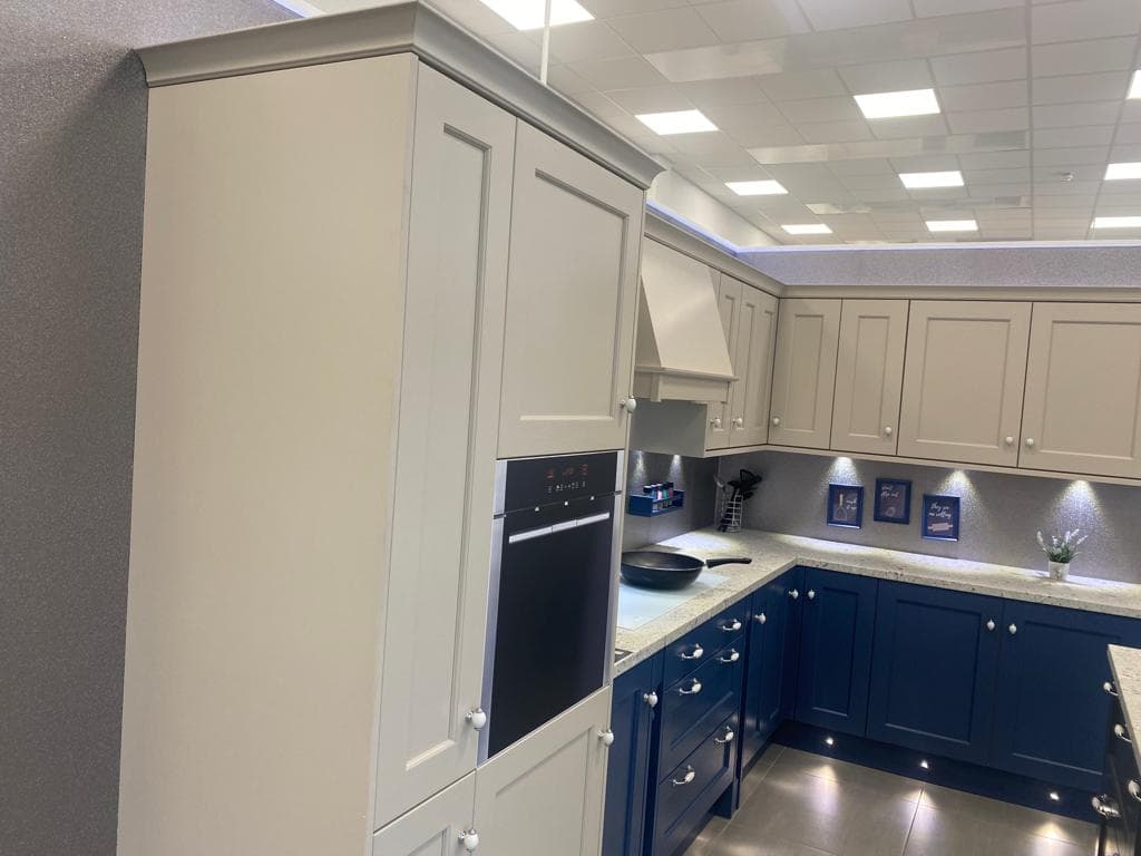 Two-tone shaker kitchen with cream upper cabinets and navy lower cabinets, stone worktop, integrated black oven, and recessed ceiling lights.