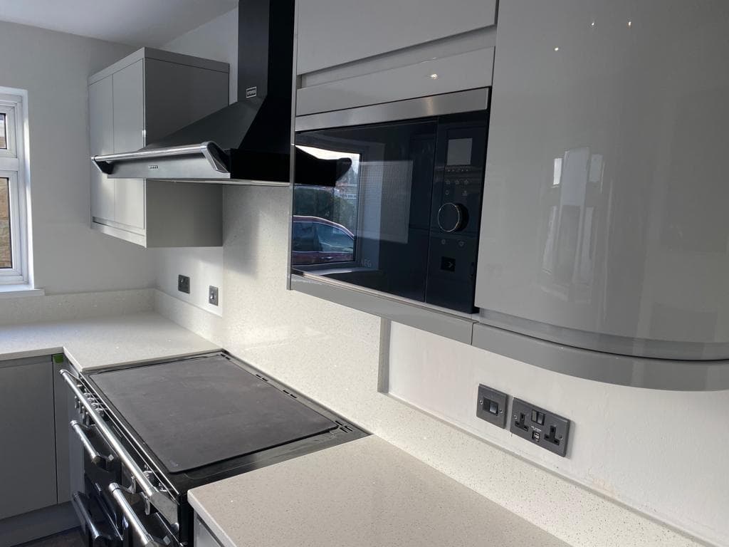 Modern kitchen with light grey and white cabinetry, white quartz worktops, black built-in oven and hob, and a curved curved island with integrated seating.